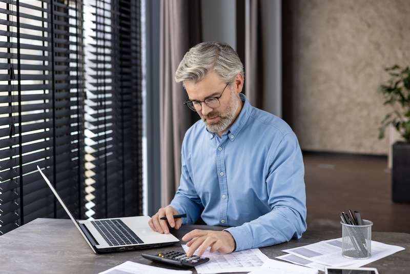 businessman using laptop and reviewing documents while working